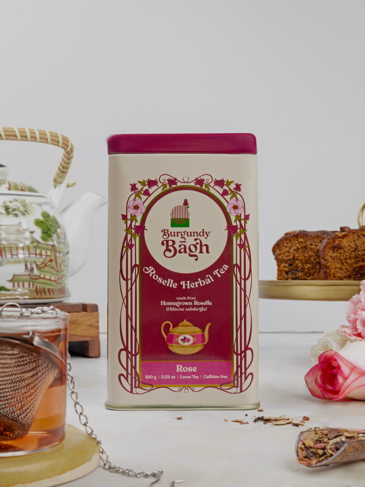 Burgundy Bagh Roselle Herbal Tea Rose tin with a glass teapot and cake