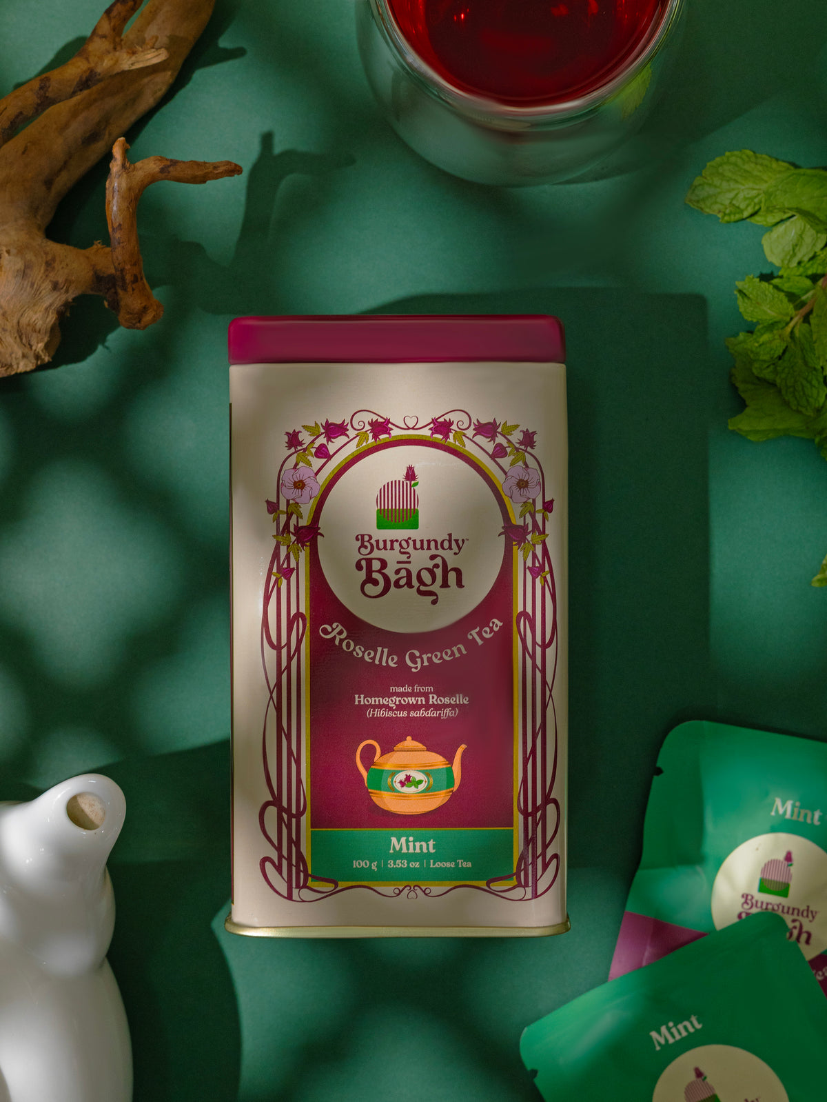 Burgundy Bagh Roselle Green Tea Mint tin with fresh mint on a green background