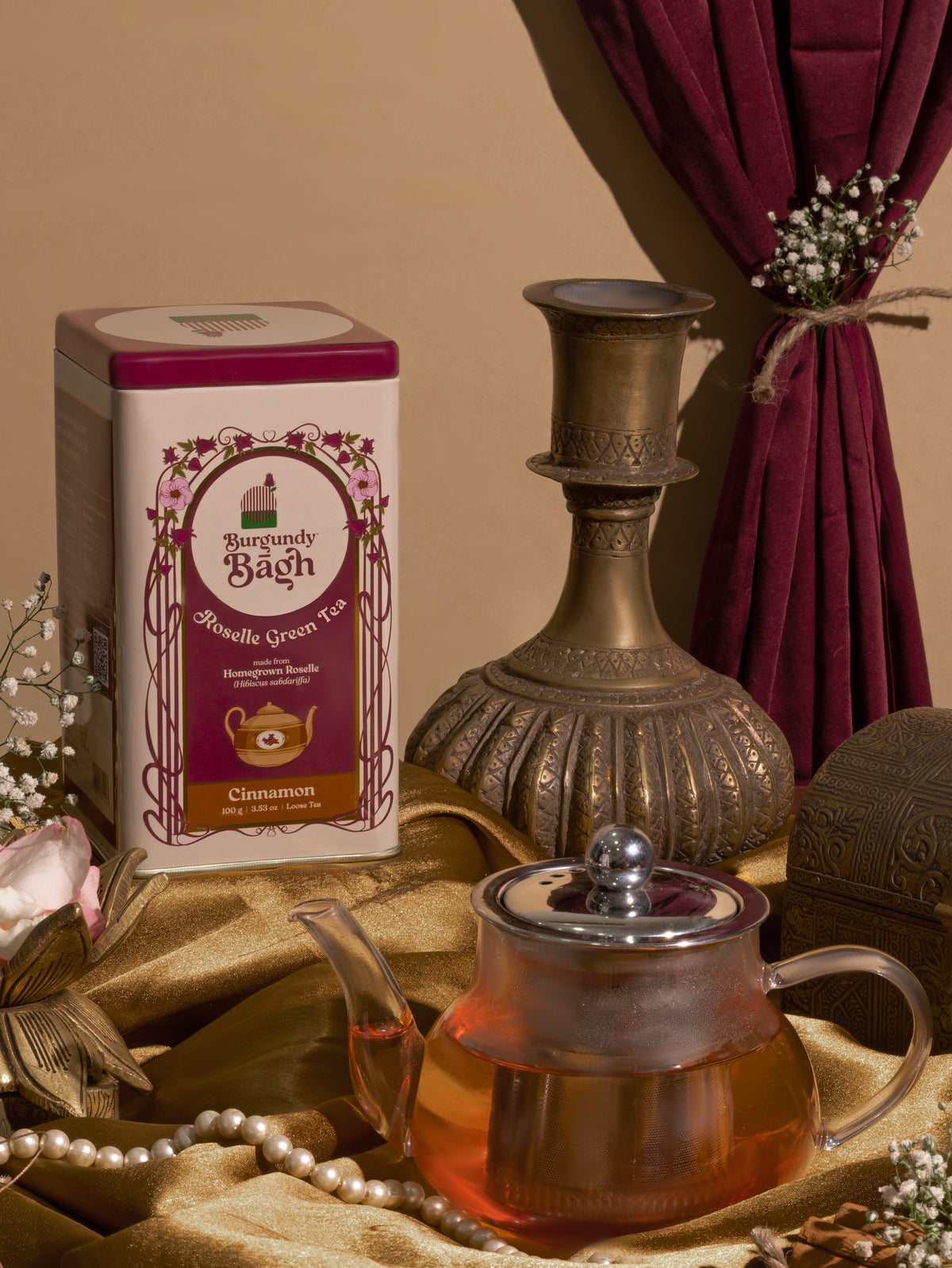 Burgundy Bagh Roselle Herbal Tea tin with a glass teapot and brass candlestick