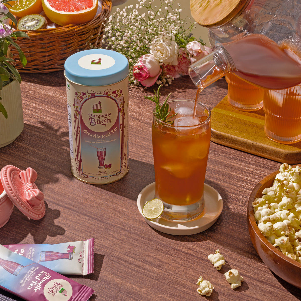 Burgundy Bagh Roselle Iced Tea poured at an outdoor table with fruit and flowers