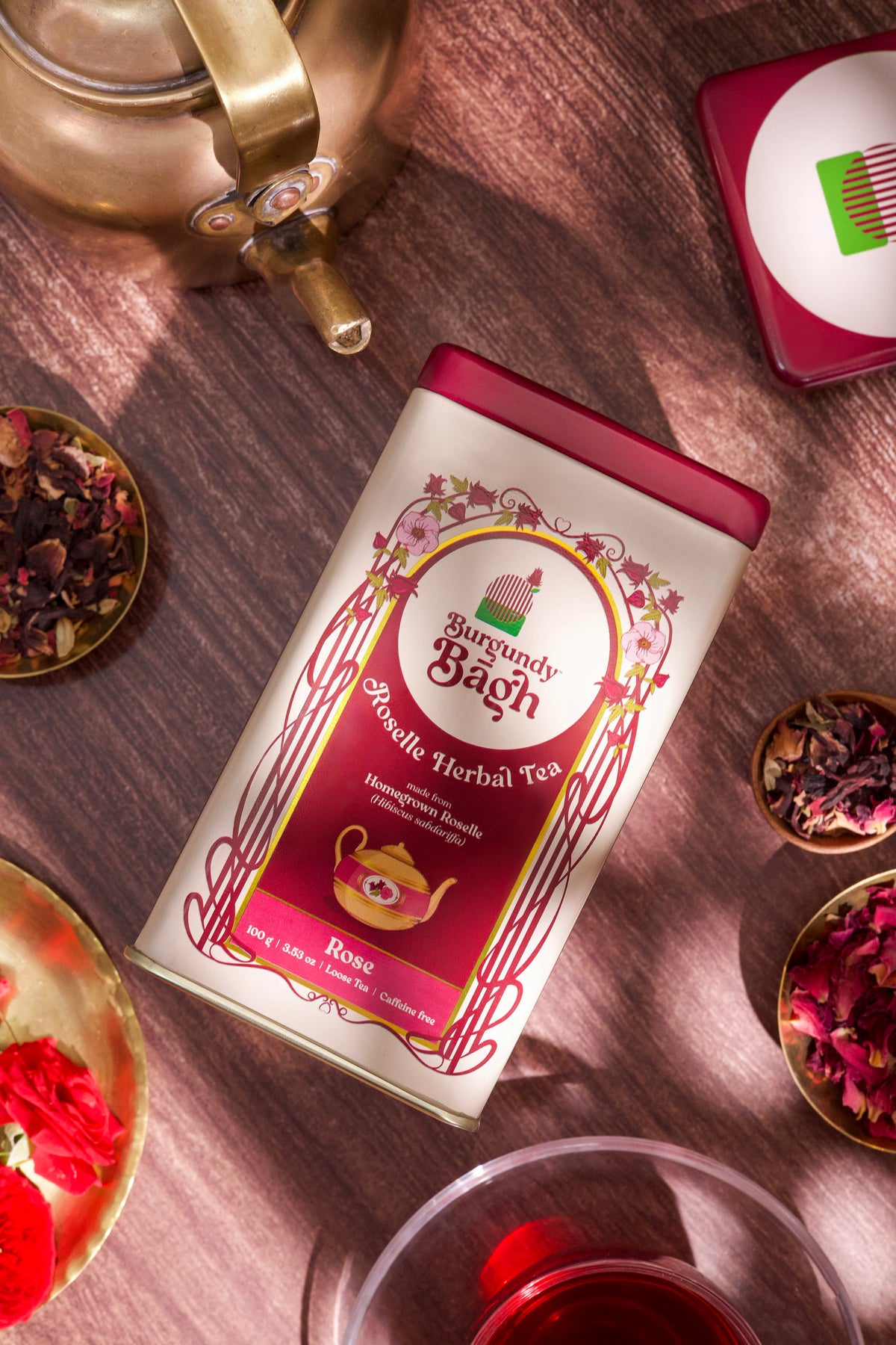 Burgundy Bagh Roselle Herbal Tea with brass kettle and brewed tea on dark wood