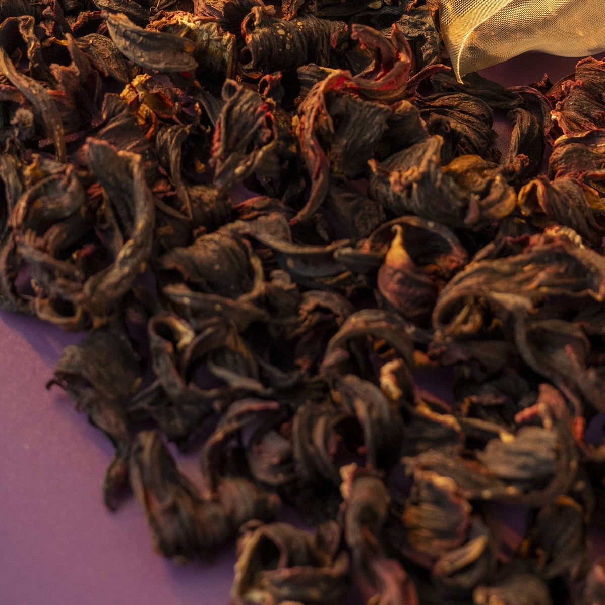 Dried roselle petals beside a pyramid tea bag